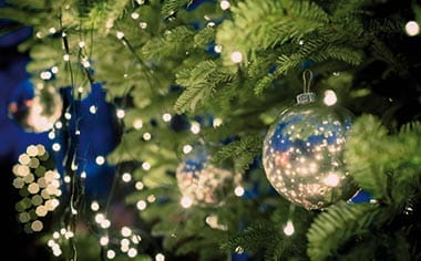 A Christmas tree lit with fairy lights and decorated with baubles A Christmas tree lit with fairy lights and decorated with baubles